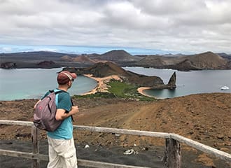 A man standing on top of a hill looking at the water.