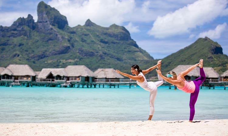 Two people are doing yoga on the beach.