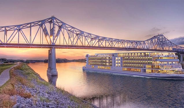 A large cruise ship on the water under a bridge.