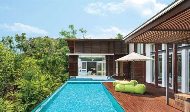 A pool with an umbrella and chairs in the background.