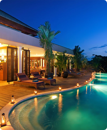 A pool with lights on and palm trees in the background.