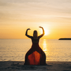 A woman in red dress on beach at sunset.