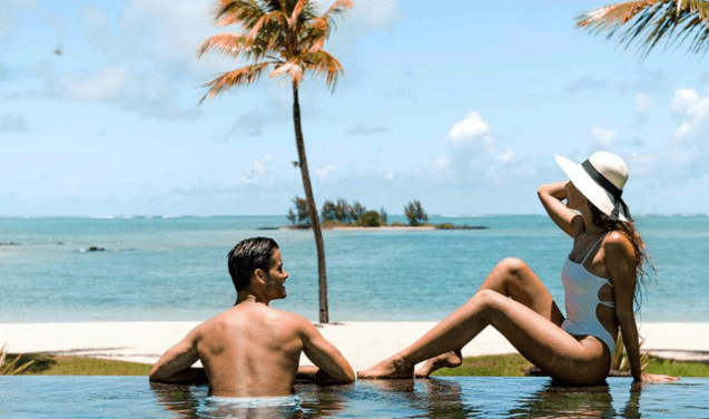 A man and woman sitting in the water at the edge of a beach.